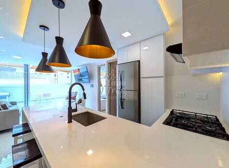 Modern cocina with white quartz countertop, black pendant lights, gas cooktop, stainless steel refrigerator, and island sink with bronze faucet.