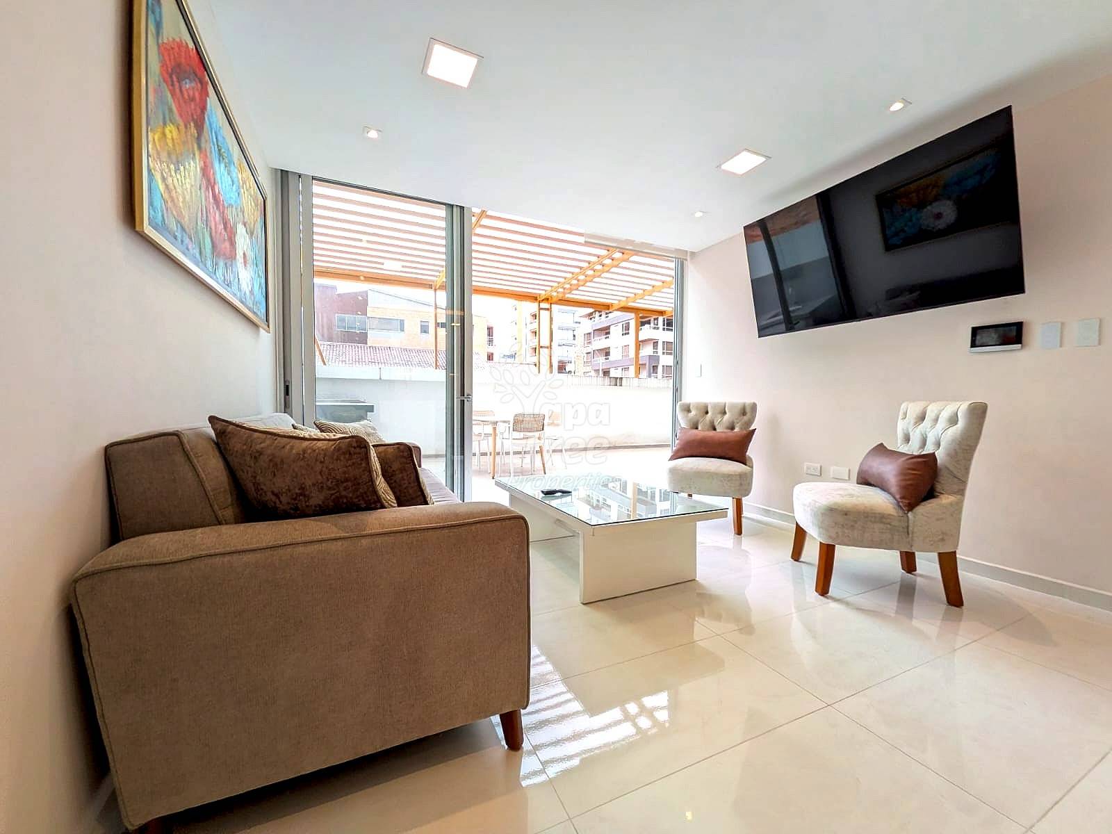 Modern living room with beige tile floors, brown sofa, cream accent chairs, glass coffee table, wall-mounted TV, and sliding glass doors opening to a terrace.