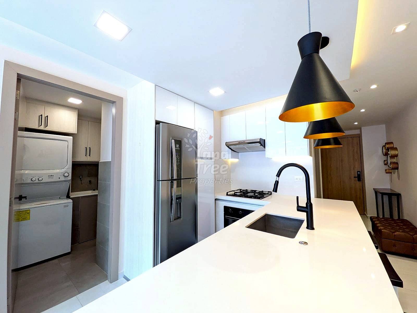 Modern cocina with white cabinetry, stainless steel appliances, quartz countertop, black pendant lights, and stacked washer-dryer unit in adjacent lavandería alcove.