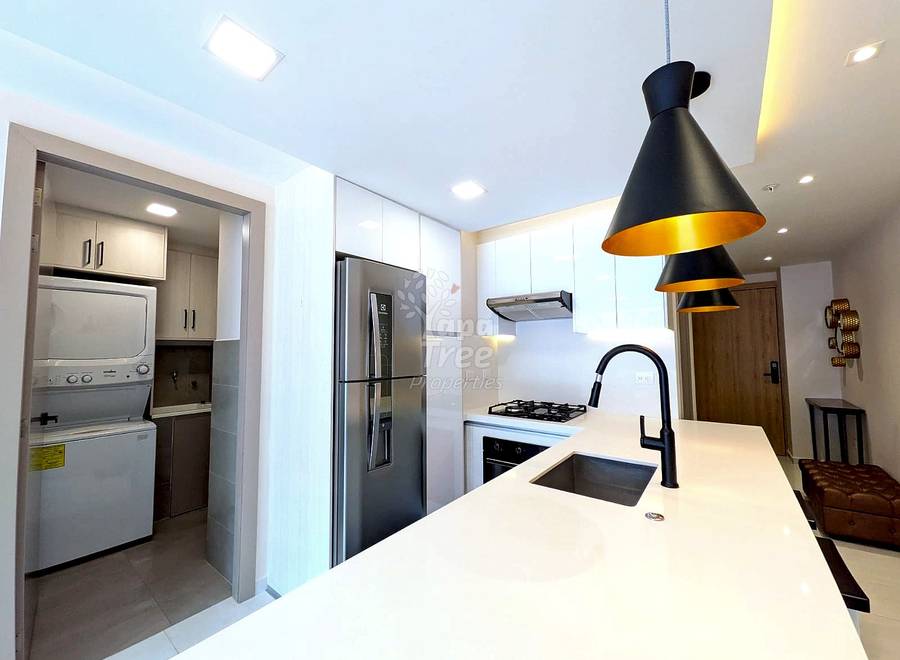 Modern cocina with white cabinetry, stainless steel appliances, quartz countertop, black pendant lights, and stacked washer-dryer unit in adjacent lavandería alcove.