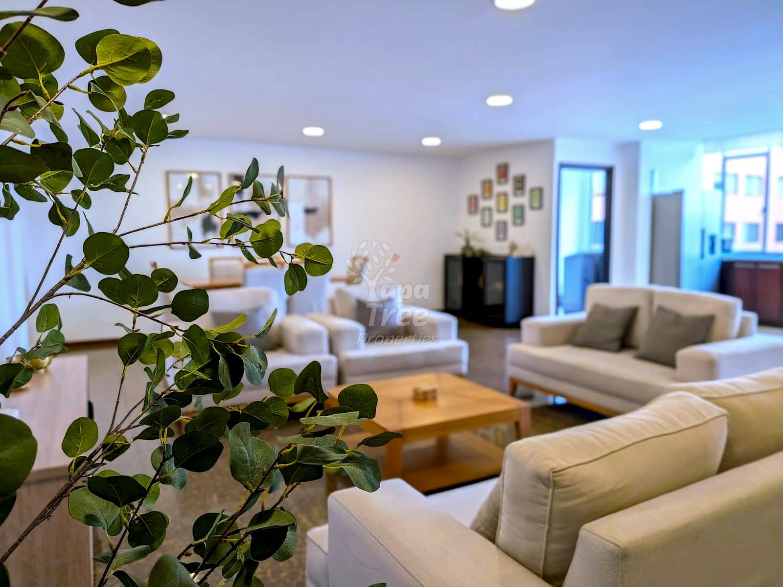 A bright living room with cream couches, dark gray cushions, wooden coffee table, and recessed lighting.