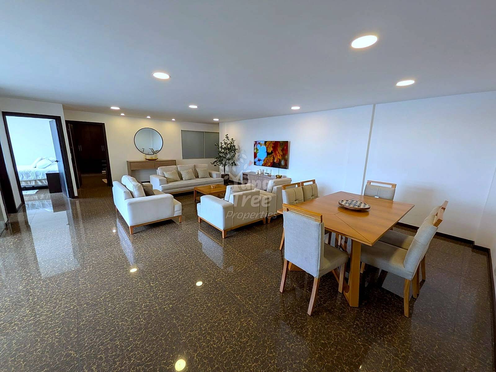 The living room and dining area with recessed lighting, brown patterned floor, white walls, and a light wood dining table.