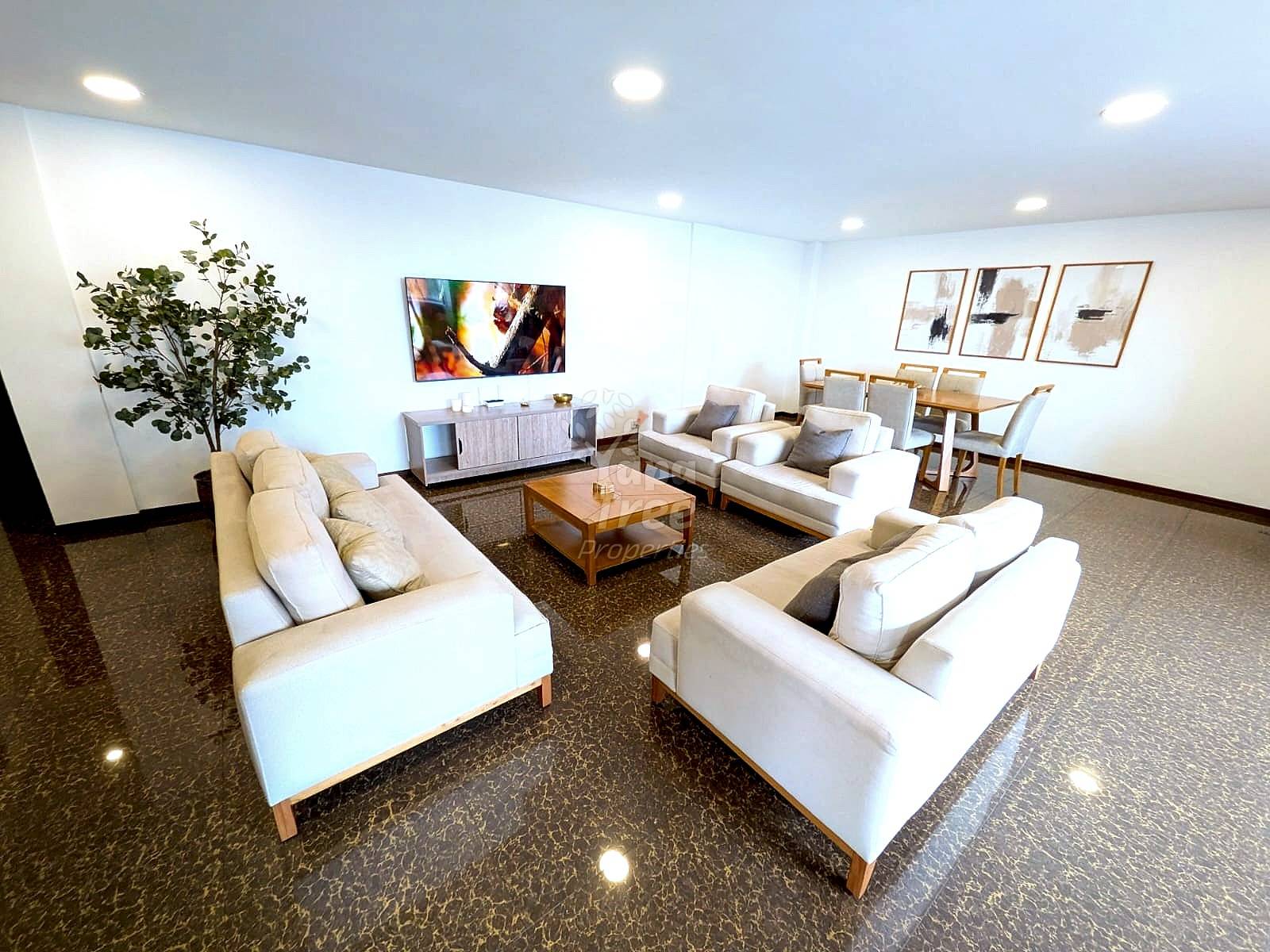 A bright living room and dining area with cream sofas, a wood coffee table, and a TV.