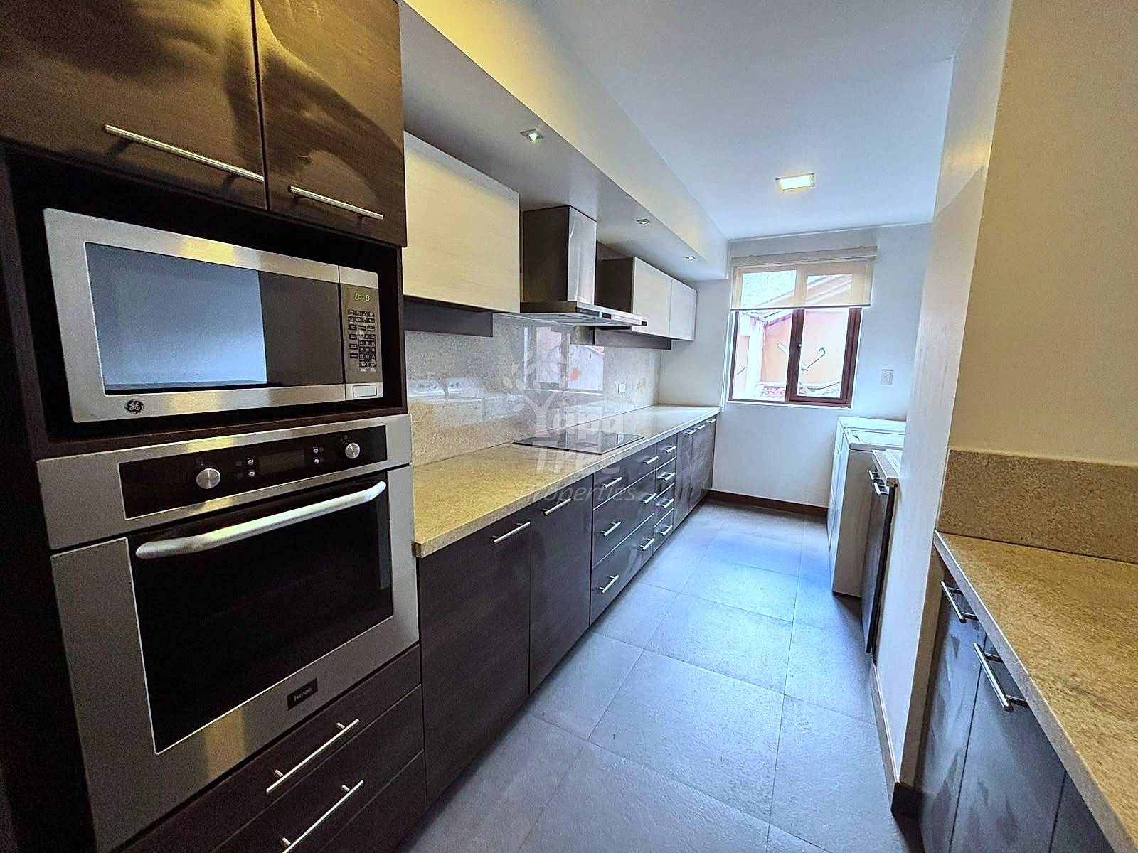 Modern kitchen with dark cabinetry, stainless steel appliances, granite countertop, tile flooring, and window with natural light.