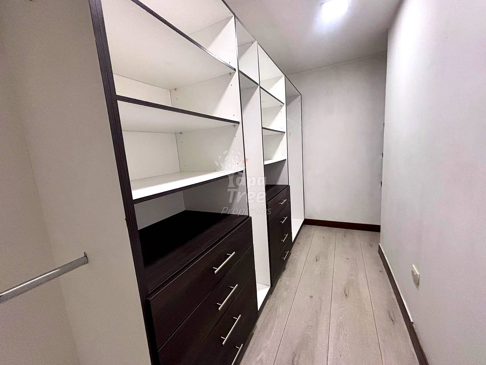 Narrow walk-in closet with black and white built-in cabinetry, white shelves, and light wood flooring throughout.