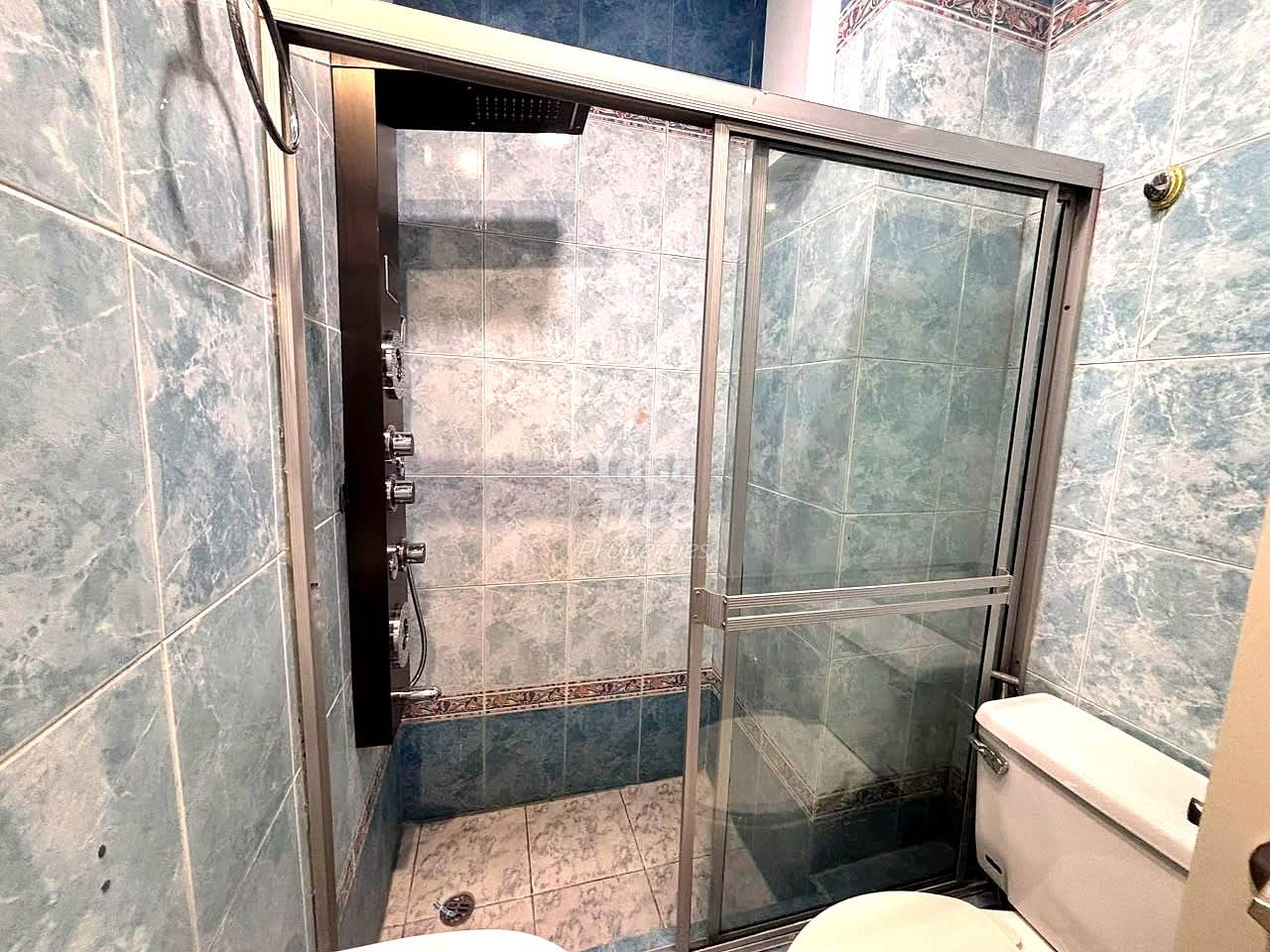 Bathroom with gray tile walls, glass shower enclosure with metal frame, and white toilet.