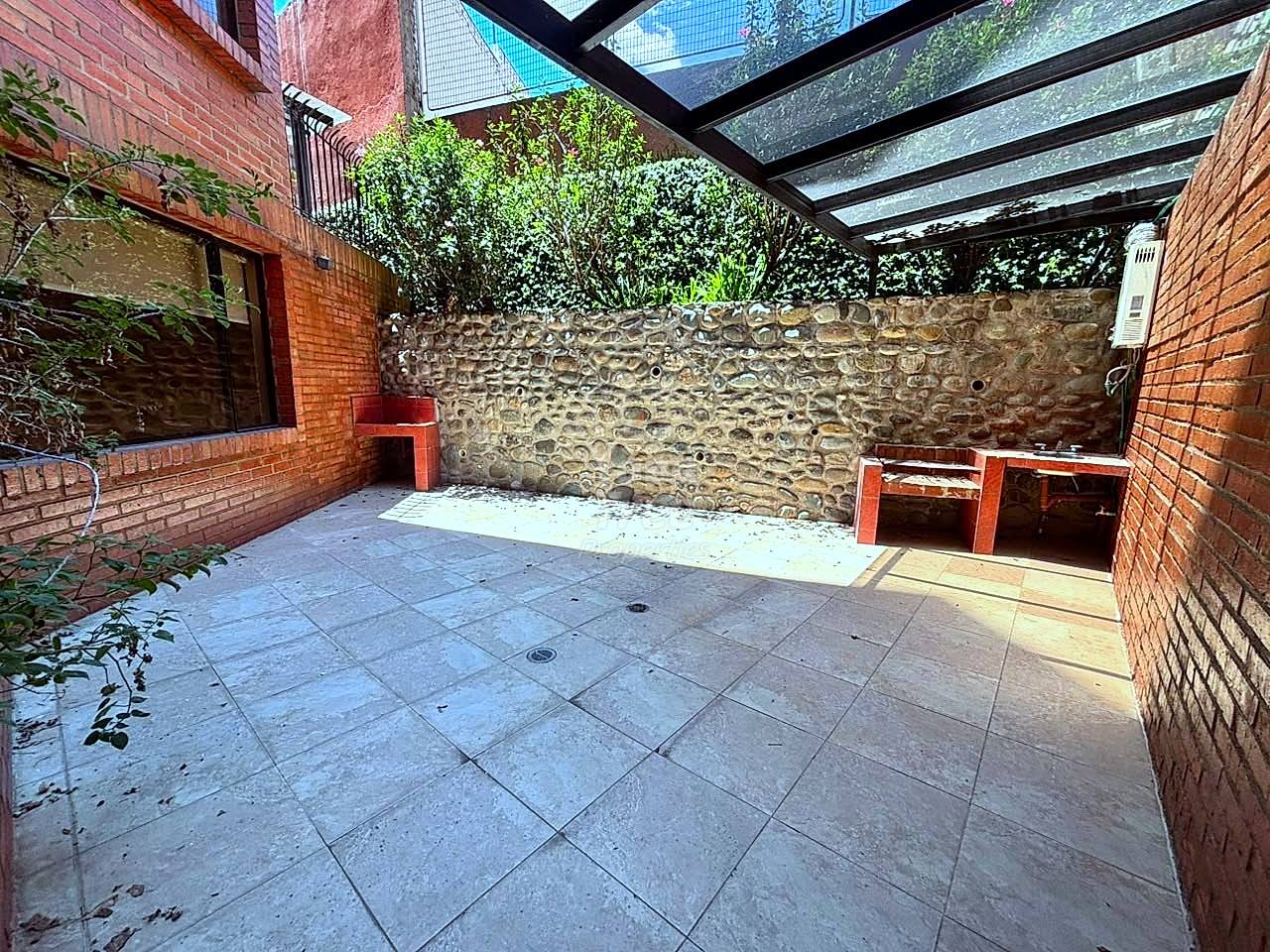 Outdoor patio with gray tile flooring, red brick walls, stone feature wall, black metal pergola with polycarbonate panels, and potted plants
