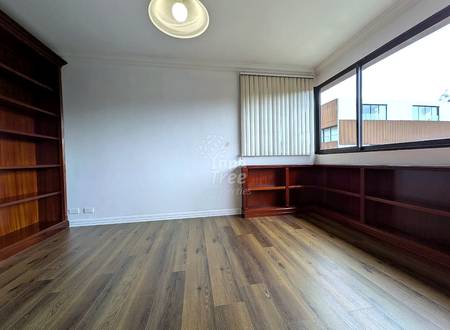 Empty room with wood laminate flooring, white walls, ceiling light fixture, large window with vertical blinds, and wooden built-in shelving units on two walls.
