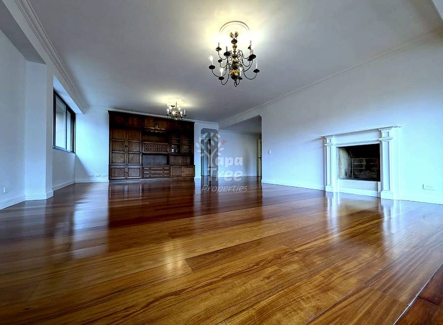 Empty living room with polished wooden flooring, ornate ceiling chandelier, built-in wood cabinetry, fireplace, and large window with natural light