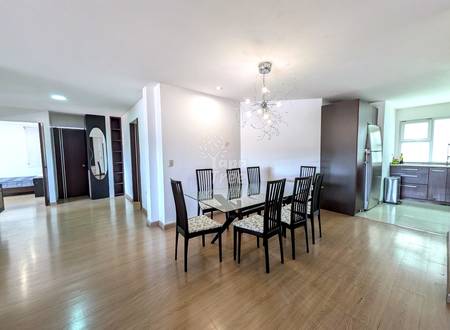 Open-plan dining and living area with wood flooring, dining table with six black chairs, modern pendant light fixture, and kitchen visible in background.
