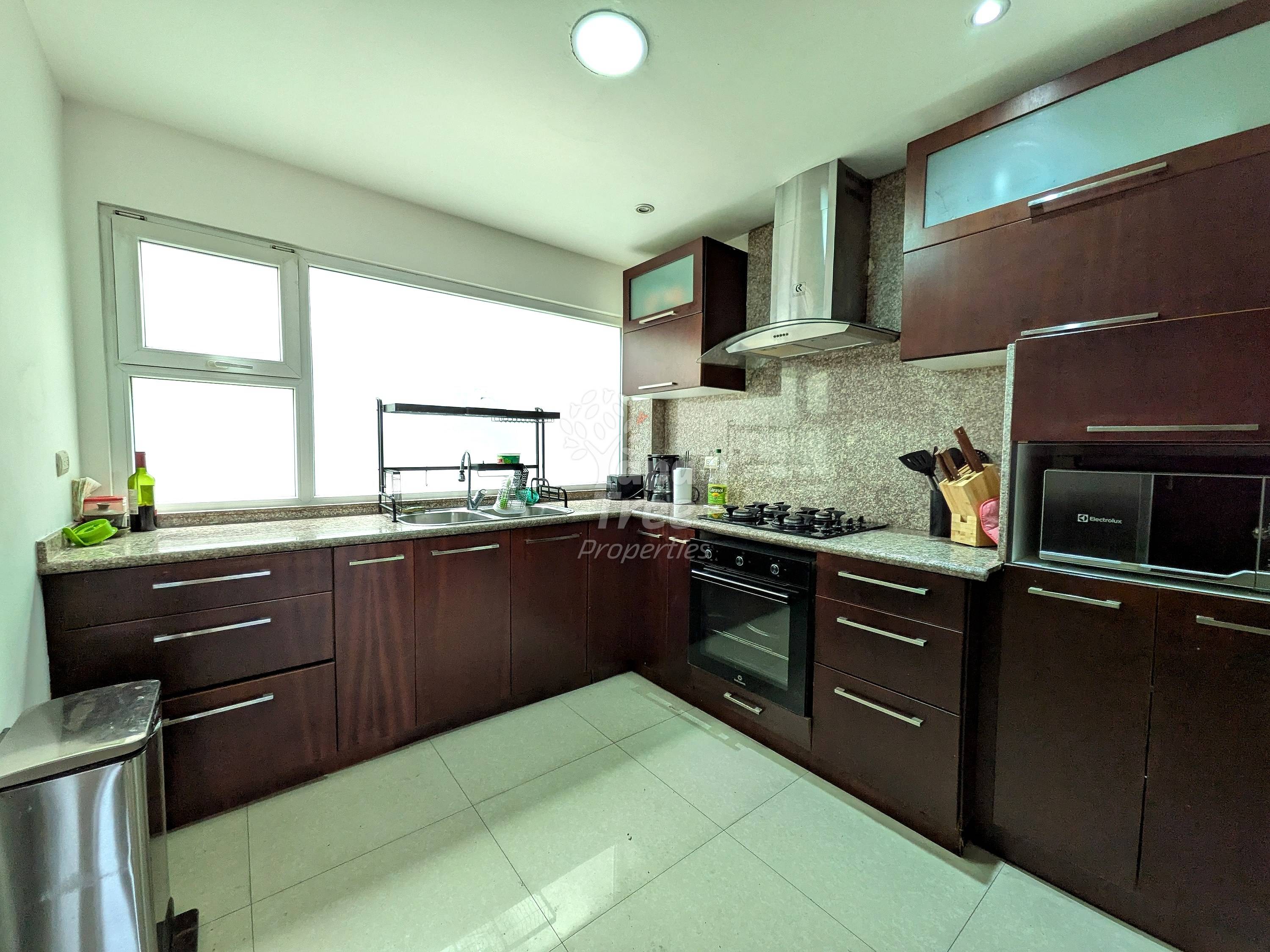 Modern cocina with dark wood cabinetry, granite countertops, gas cooktop, electric oven, and large windows providing natural light over tile flooring.