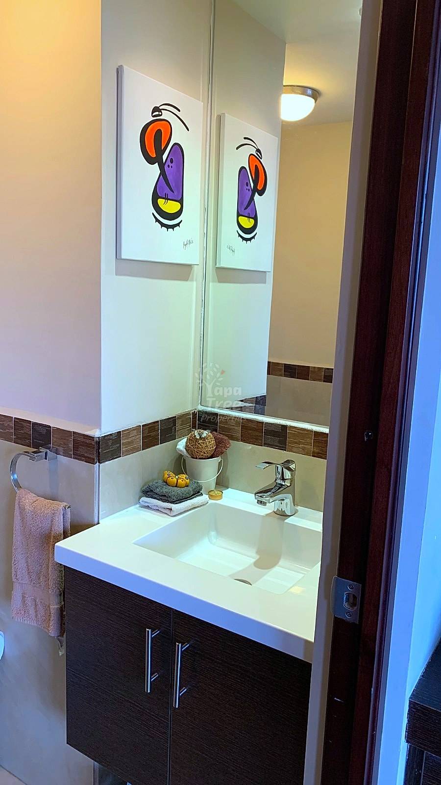 Bathroom with white sink, dark wood vanity, large mirror with colorful bird artwork, brown tile trim, and ceiling light.