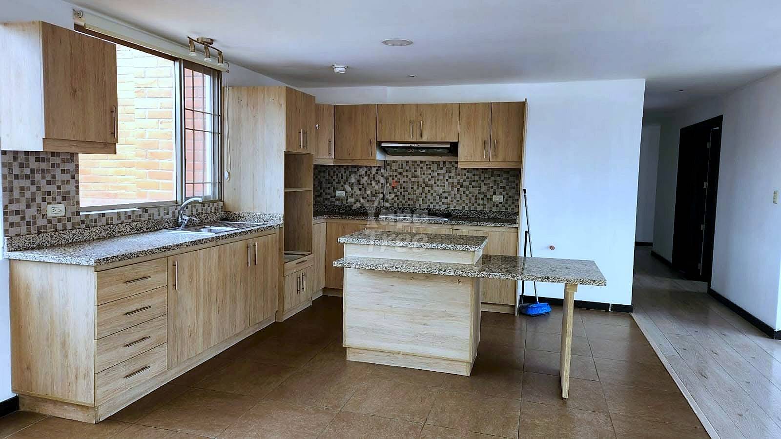 Open-plan cocina with light wood cabinets, granite countertops, mosaic tile backsplash, center island, and brown tile flooring throughout.