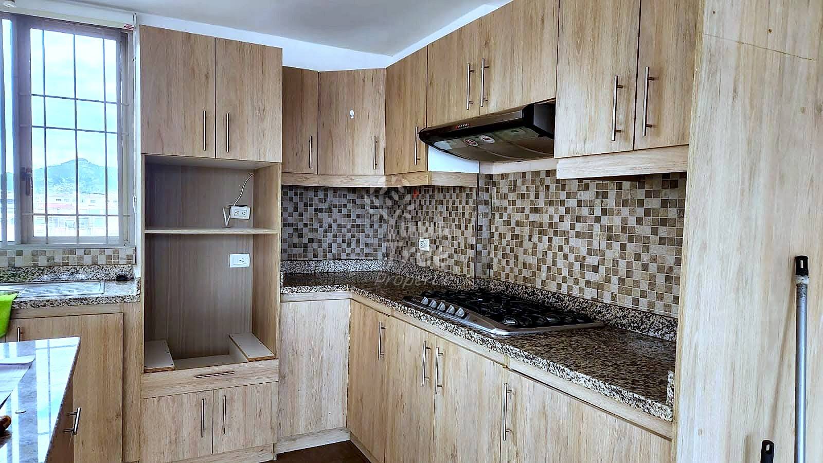 Modern kitchen with light wood cabinetry, granite countertops, mosaic tile backsplash, gas stovetop, black range hood, and window with mountain view.