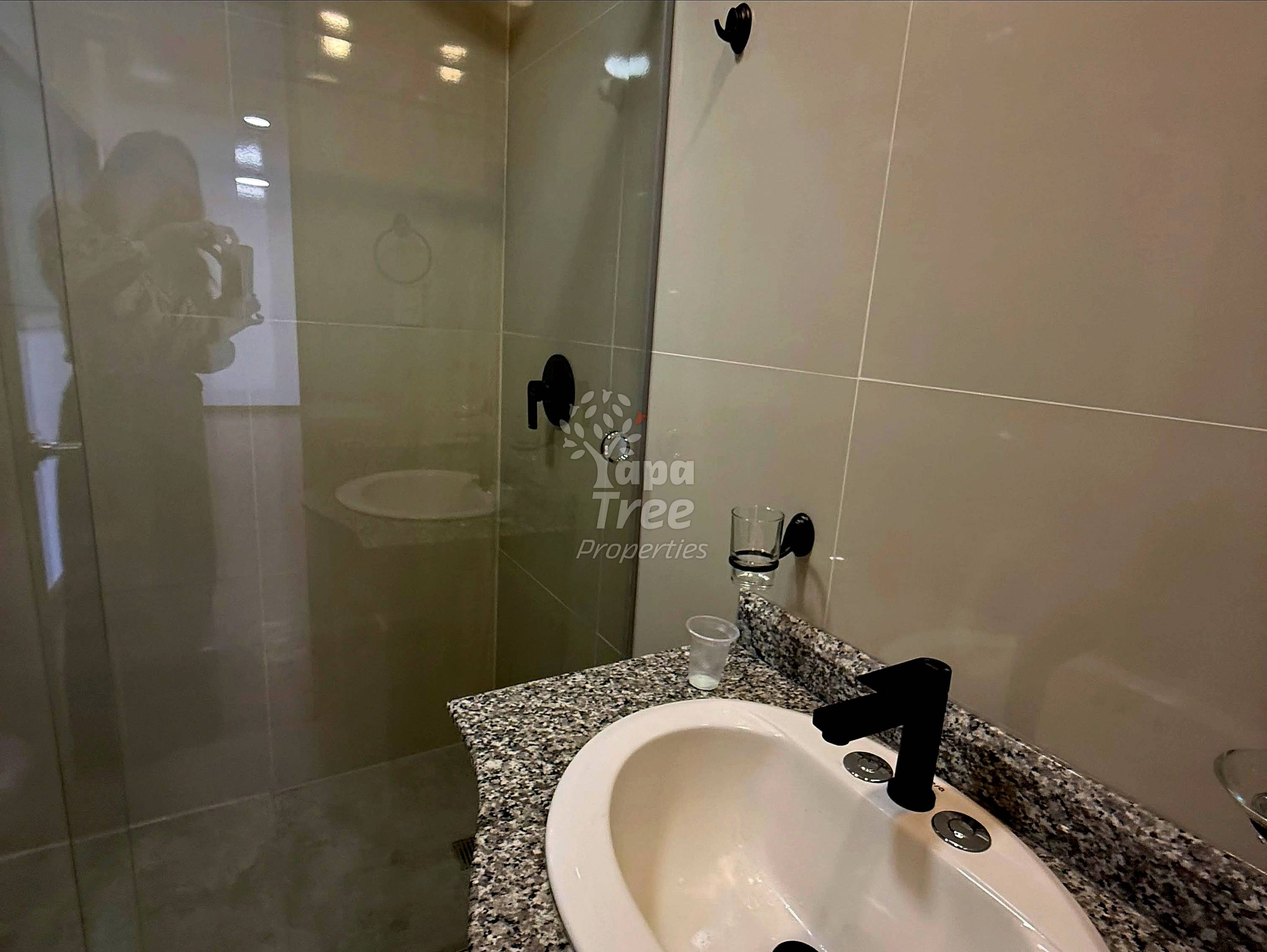 Modern bathroom with granite countertop, white round sink, black faucet, and glass shower enclosure with rainfall showerhead.