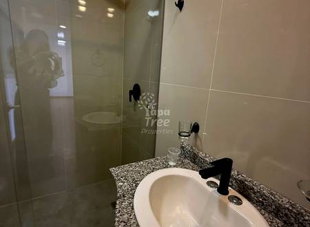 Modern bathroom with granite countertop, white round sink, black faucet, and glass shower enclosure with rainfall showerhead.