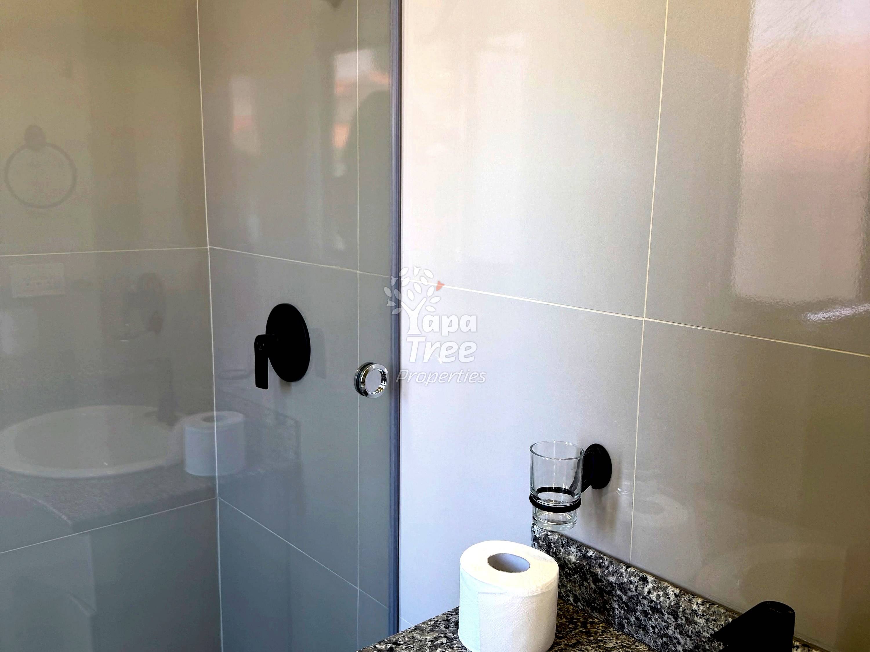 Bathroom with ceramic tile walls, glass shower enclosure with black handle, granite countertop, and toilet paper roll.