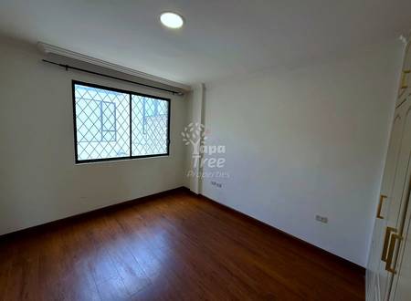Empty bedroom with dark wood flooring, white walls, barred window with black frame, and recessed ceiling light.
