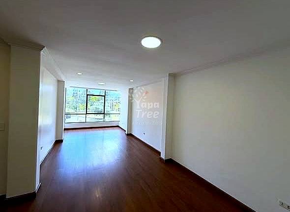 Empty room with dark wood flooring, white walls, recessed ceiling lights, and large window with city views.