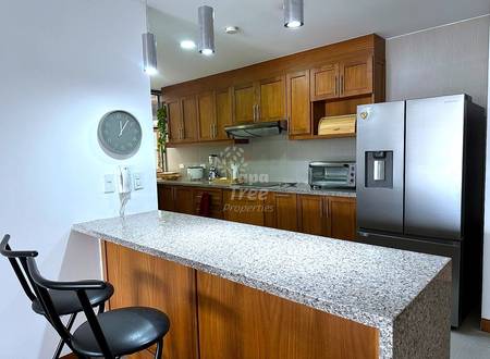 Modern cocina with wood cabinetry, granite countertops, stainless steel refrigerator, pendant lighting, and island seating with black chairs.