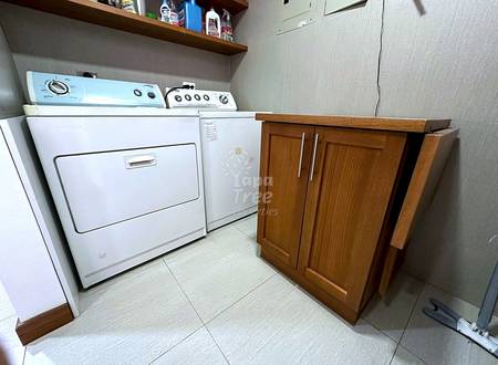 Lavandería with white dryer and washing machine, wooden cabinet, tiled floor, wall shelving with cleaning supplies.