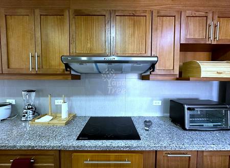 Kitchen with wood cabinets, granite countertop, induction cooktop, range hood, and stainless steel appliances under bright overhead lighting.