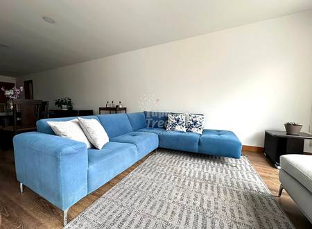 Living room with blue sectional sofa, patterned area rug, wooden flooring, white walls, and recessed ceiling lights.