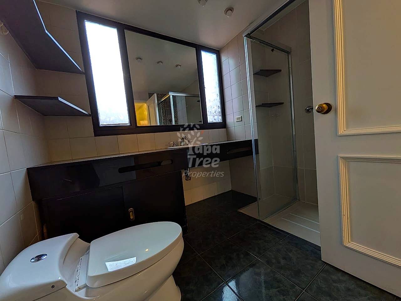 Modern bathroom with black granite floor, white toilet, black vanity with sink, large illuminated mirror, glass shower enclosure, and tiled walls.