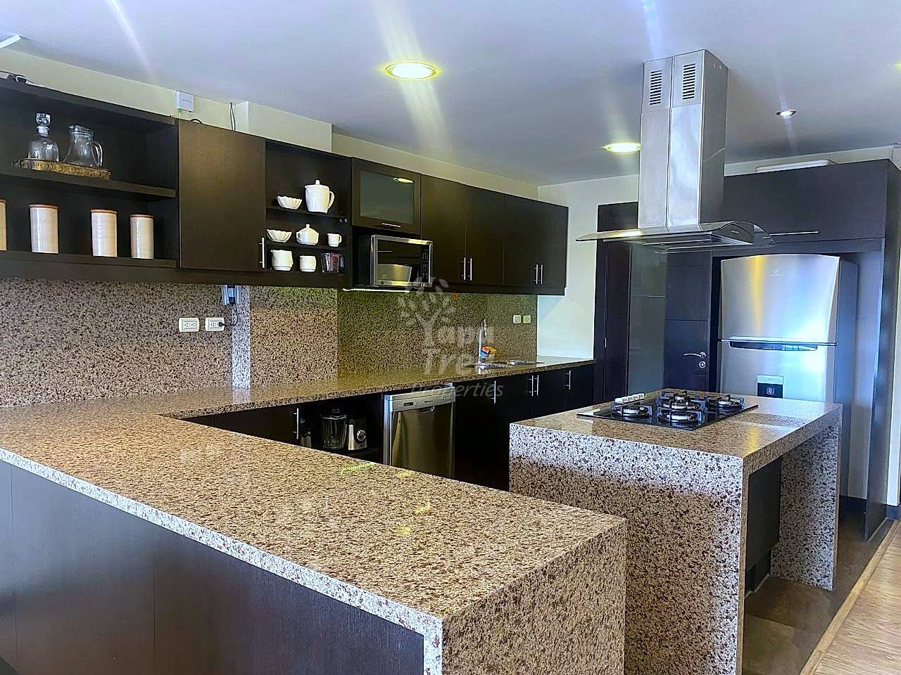 A modern kitchen with dark wood cabinets, speckled granite countertops, and stainless steel appliances.