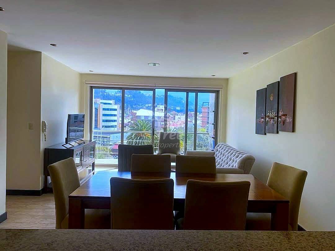Dining room and living area with a brown table, chairs, sofa, and a large window.