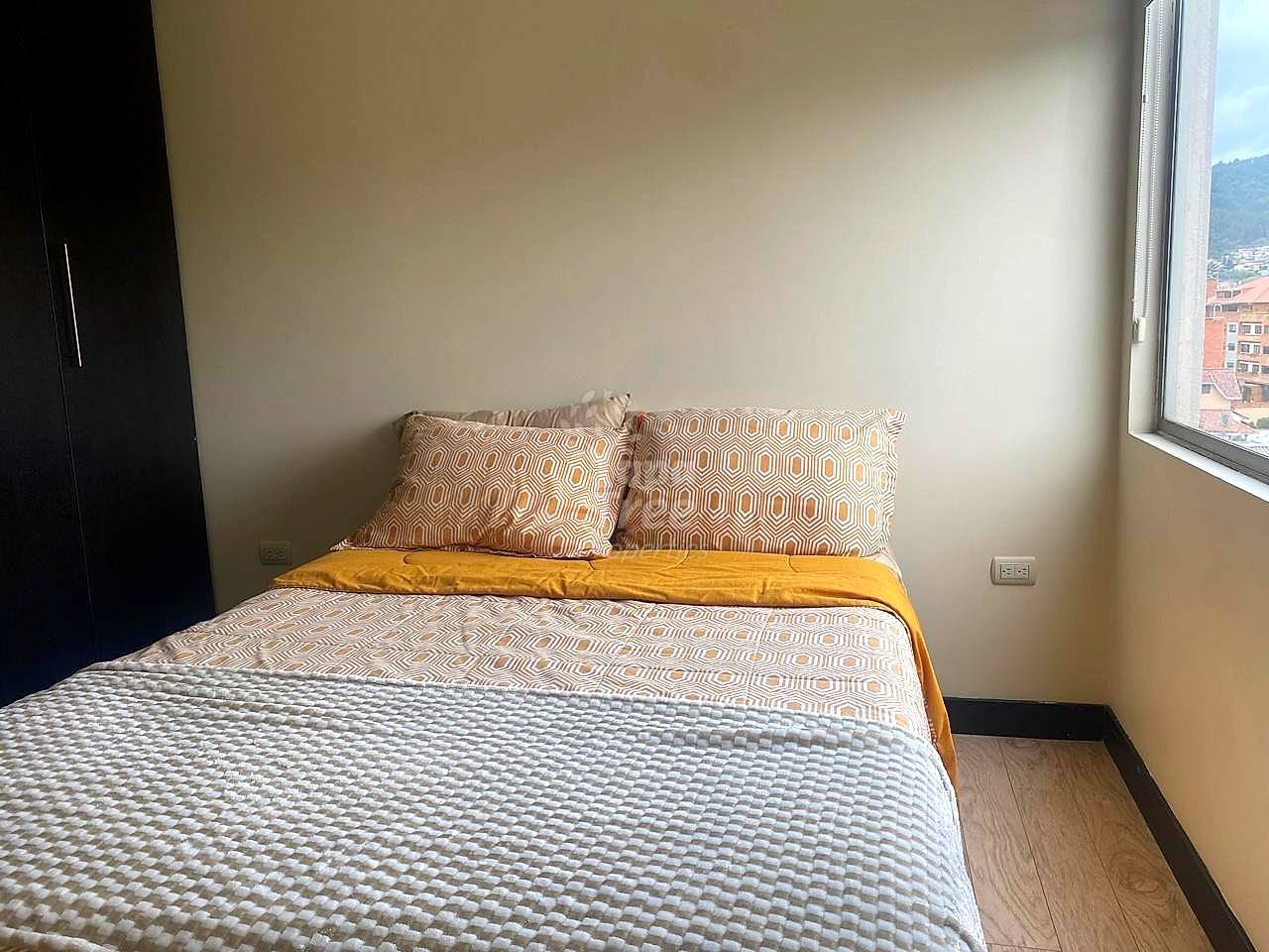 Bedroom with wooden floors, neutral walls, dark wardrobe, and geometric patterned bedding by a window.
