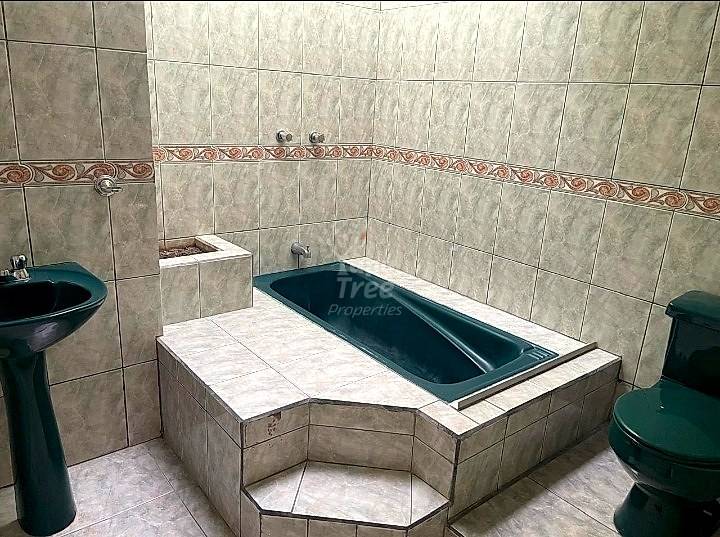Bathroom with gray ceramic tile walls, decorative border, built-in bathtub with dark blue interior, pedestal sink, and toilet.