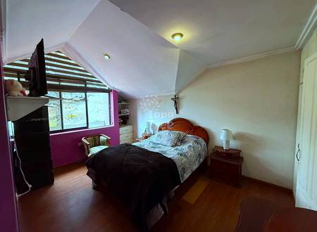 Bedroom with wooden bed frame, patterned bedding, nightstands with lamps, burgundy accent wall, angled ceiling with recessed lighting, and large window.