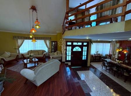 Open living room with cream-colored sofas, wooden floor, yellow walls, pendant lights, and dark entry door with transom window.