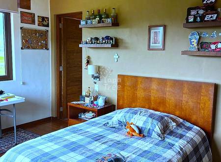 Bedroom with wooden bed frame, plaid bedding, exposed ceiling beams, yellow walls, wooden shelves, and desk area with natural light.