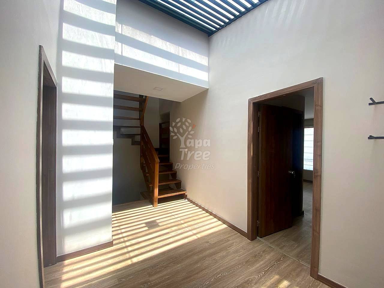 Open living area with wooden staircase, wood plank flooring, white walls, and striped skylight casting natural light from above.