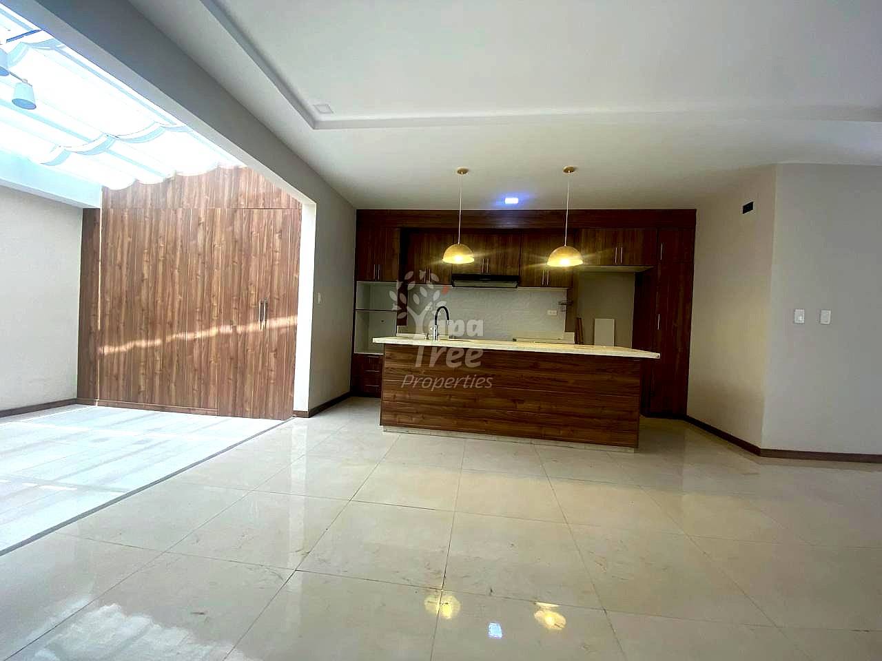 Open-concept departamento with polished light tile flooring, wood-grain island counter, dark wood cabinetry, stainless steel appliances, and skylight providing natural light.