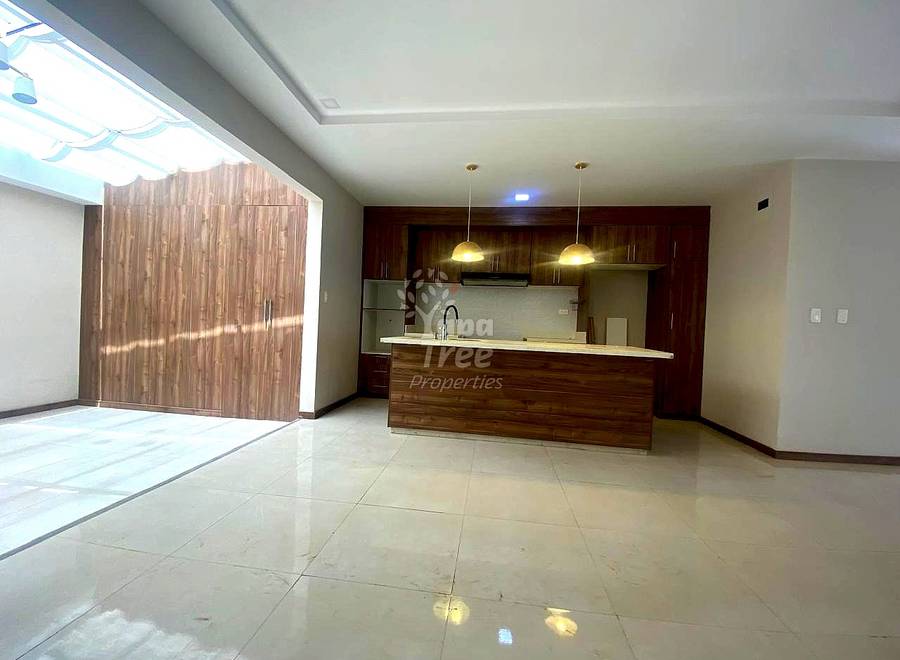 Open-concept departamento with polished light tile flooring, wood-grain island counter, dark wood cabinetry, stainless steel appliances, and skylight providing natural light.