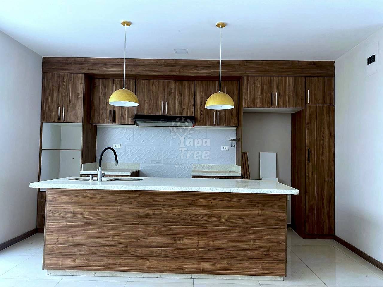 Kitchen with wood cabinets and island, granite countertop, two pendant lights, and tiled backsplash.