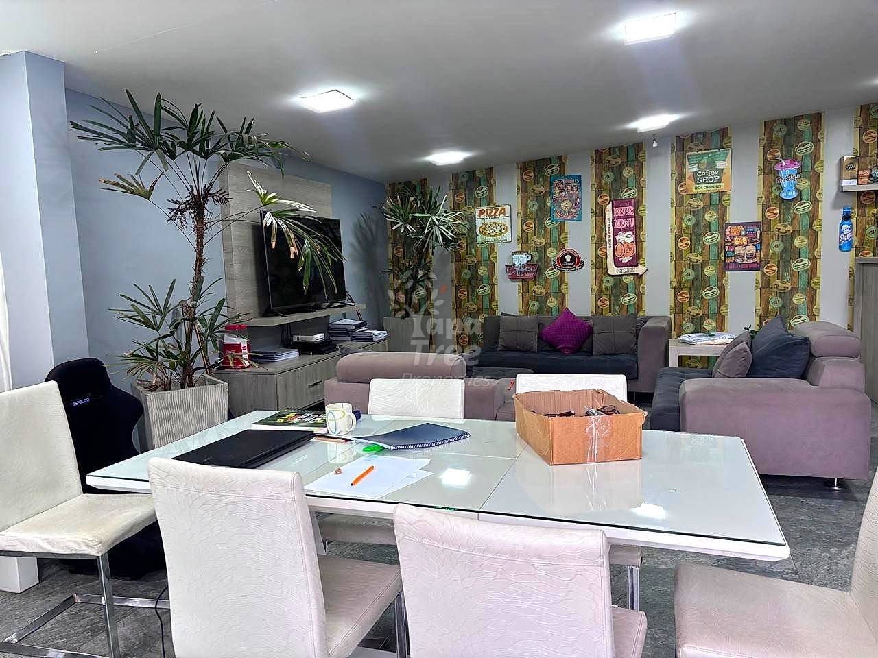 Open living room with gray sofa, white dining table, potted plants, wall-mounted TV, cactus-patterned wallpaper, and recessed ceiling lights.