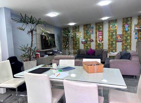 Open living room with gray sofa, white dining table, potted plants, wall-mounted TV, cactus-patterned wallpaper, and recessed ceiling lights.