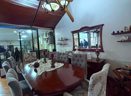 Dining room with wooden vaulted ceiling, dark wood table, upholstered chairs, pendant lighting, and framed mirror on white walls.