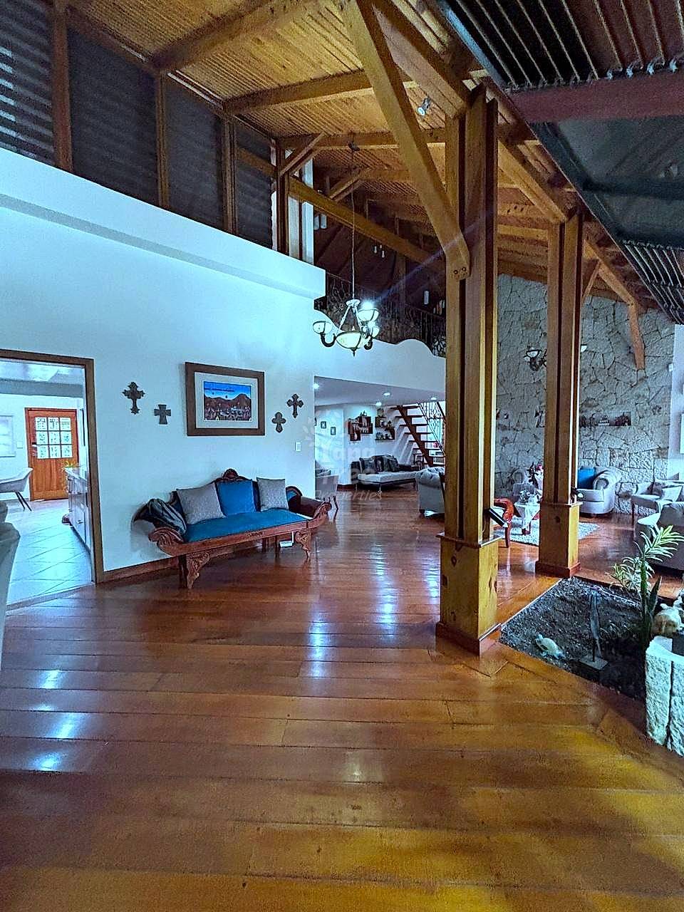 Open-plan living area with high wood beam ceilings, wooden columns, terracotta tile flooring, and upholstered bench seating with blue accents.