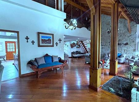 Open-plan living area with high wood beam ceilings, wooden columns, terracotta tile flooring, and upholstered bench seating with blue accents.
