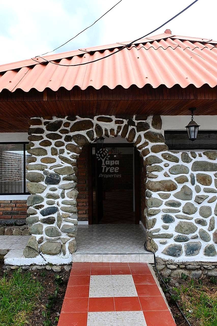 Stone and brick exterior entrance with corrugated metal roof, wooden soffit, hanging lantern, and tile walkway.