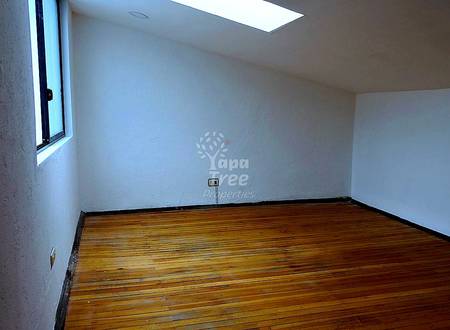 Empty room with white walls, wooden floor, small window with black frame, and single electrical outlet.