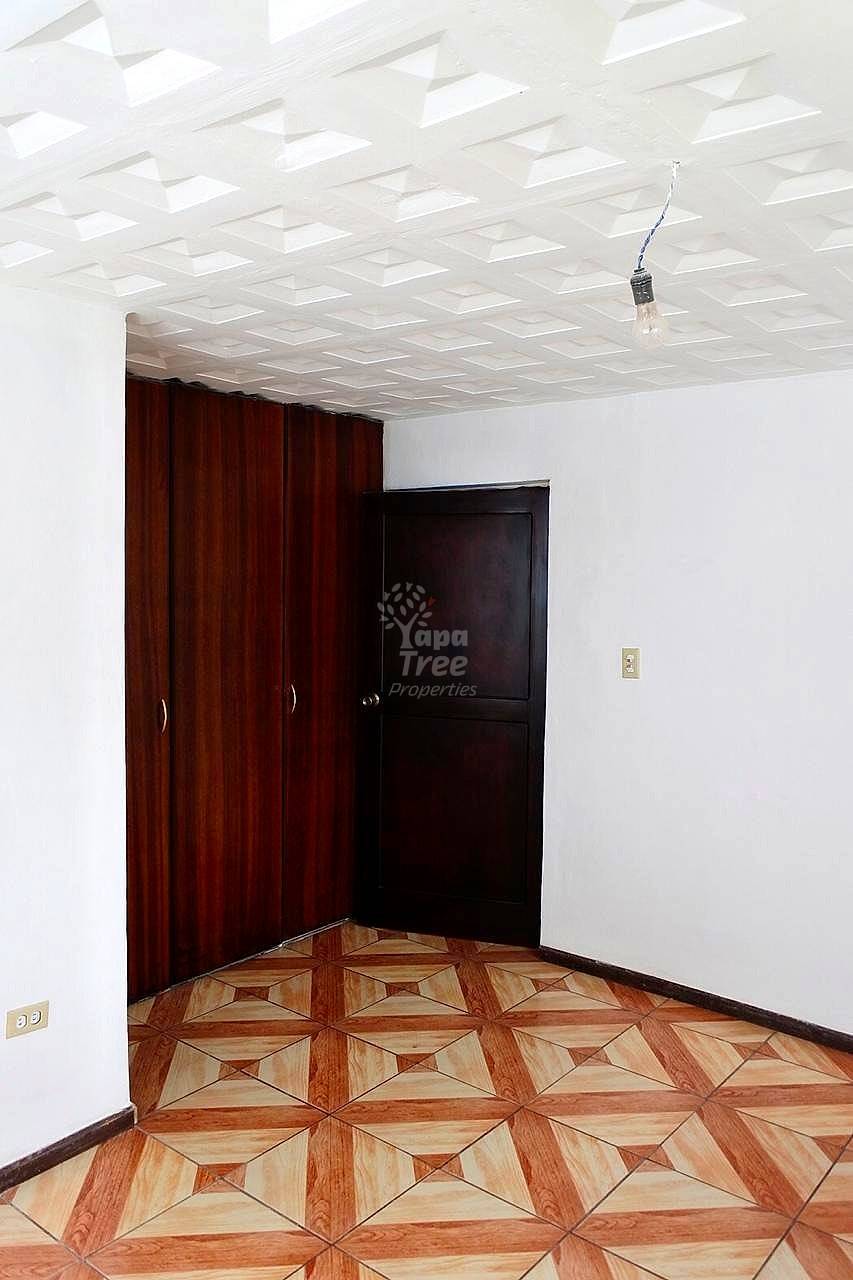 Bedroom with geometric wood floor, dark wood wardrobe, black door, white walls, and recessed ceiling lights.
