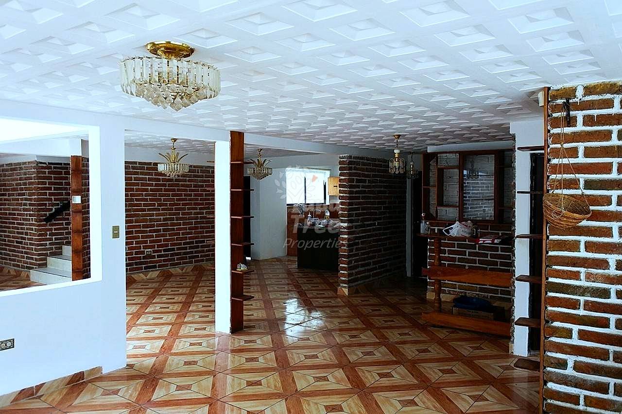 Open floor plan with geometric wood and terracotta tile flooring, exposed brick walls, white columns, crystal chandeliers, and natural light from windows.