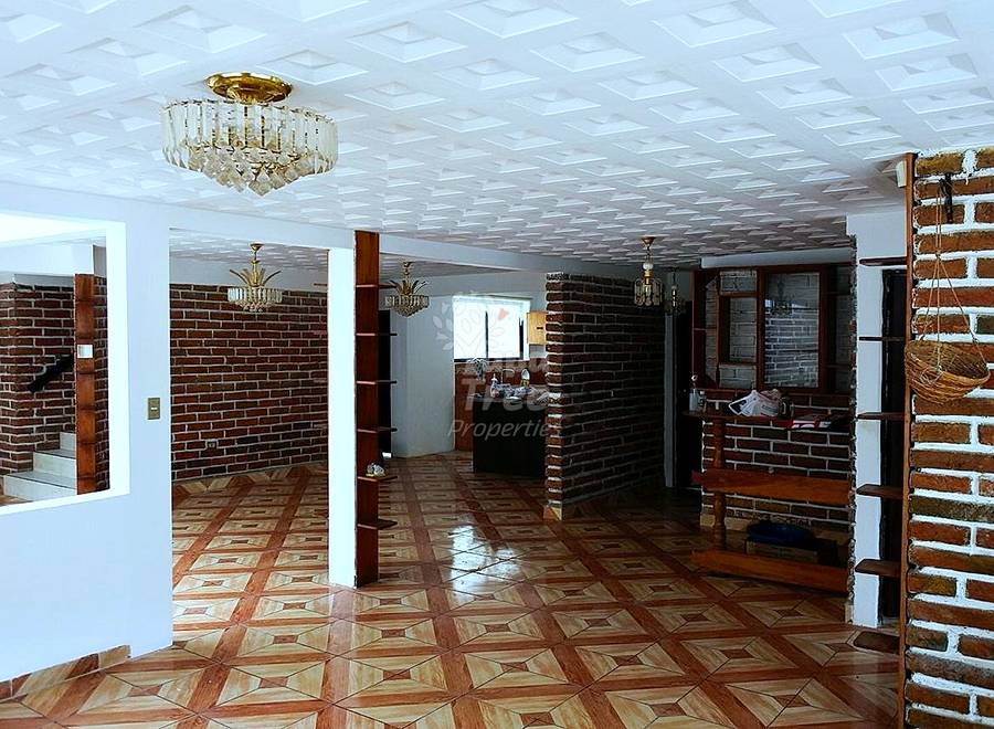 Open floor plan with geometric wood and terracotta tile flooring, exposed brick walls, white columns, crystal chandeliers, and natural light from windows.