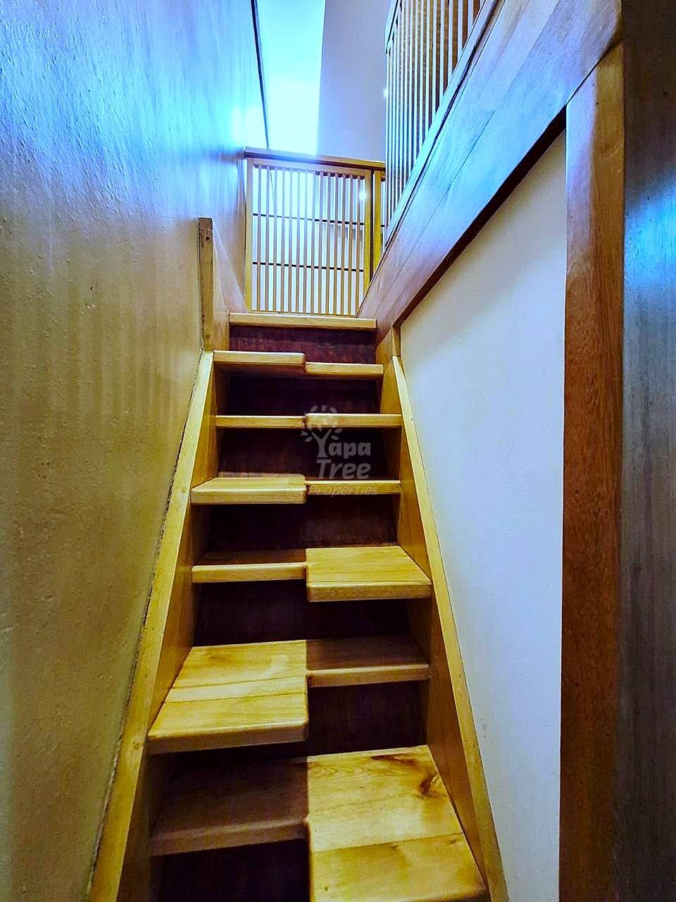 Wooden staircase with natural light from skylight above, metal railing, and textured walls on either side.